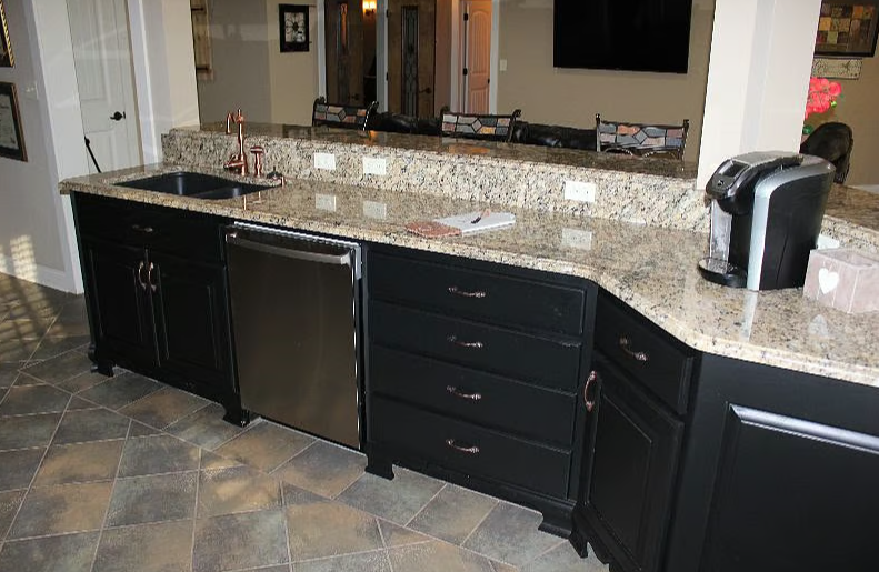Kitchen counter with black cabinets, granite countertop, stainless steel mini fridge, coffee maker, sink, and tiled floor.