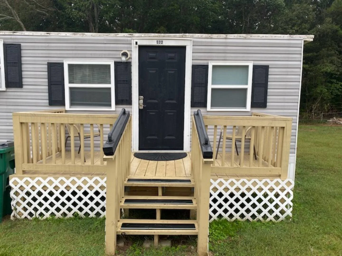 Small house with a black door, beige wooden porch with steps, and two windows with black shutters.