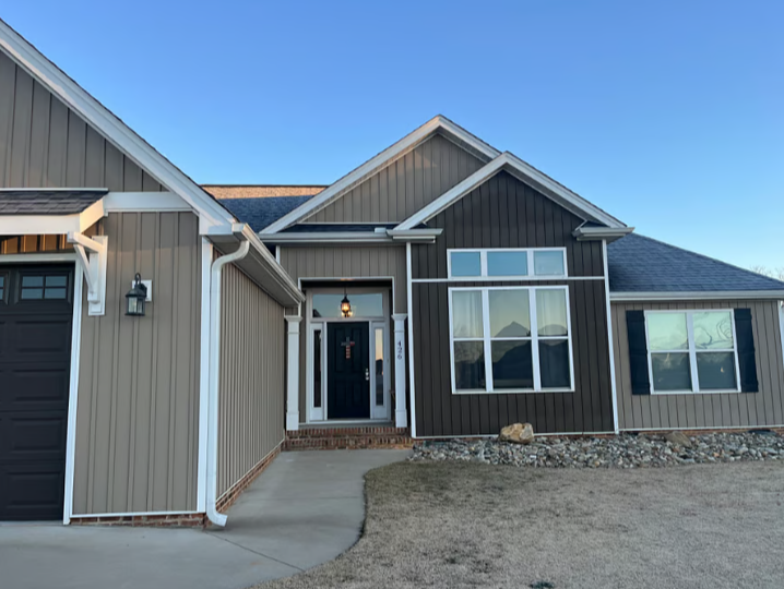 Front view of a modern house with dark and light gray exterior siding, black front door, and large front windows, under a clear blue sky.