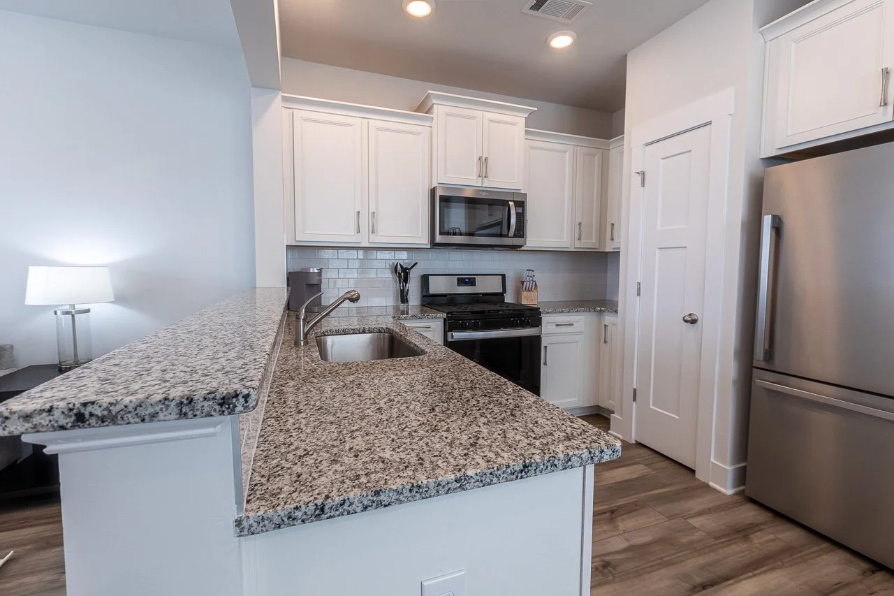 Modern kitchen with white cabinets, granite countertops, stainless steel appliances, and a small lamp on the counter.