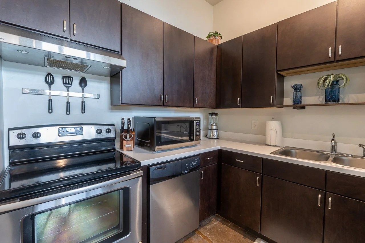 Kitchen with dark brown cabinets, stainless steel stove, microwave, dishwasher, double sink, and various kitchen appliances on the countertop.