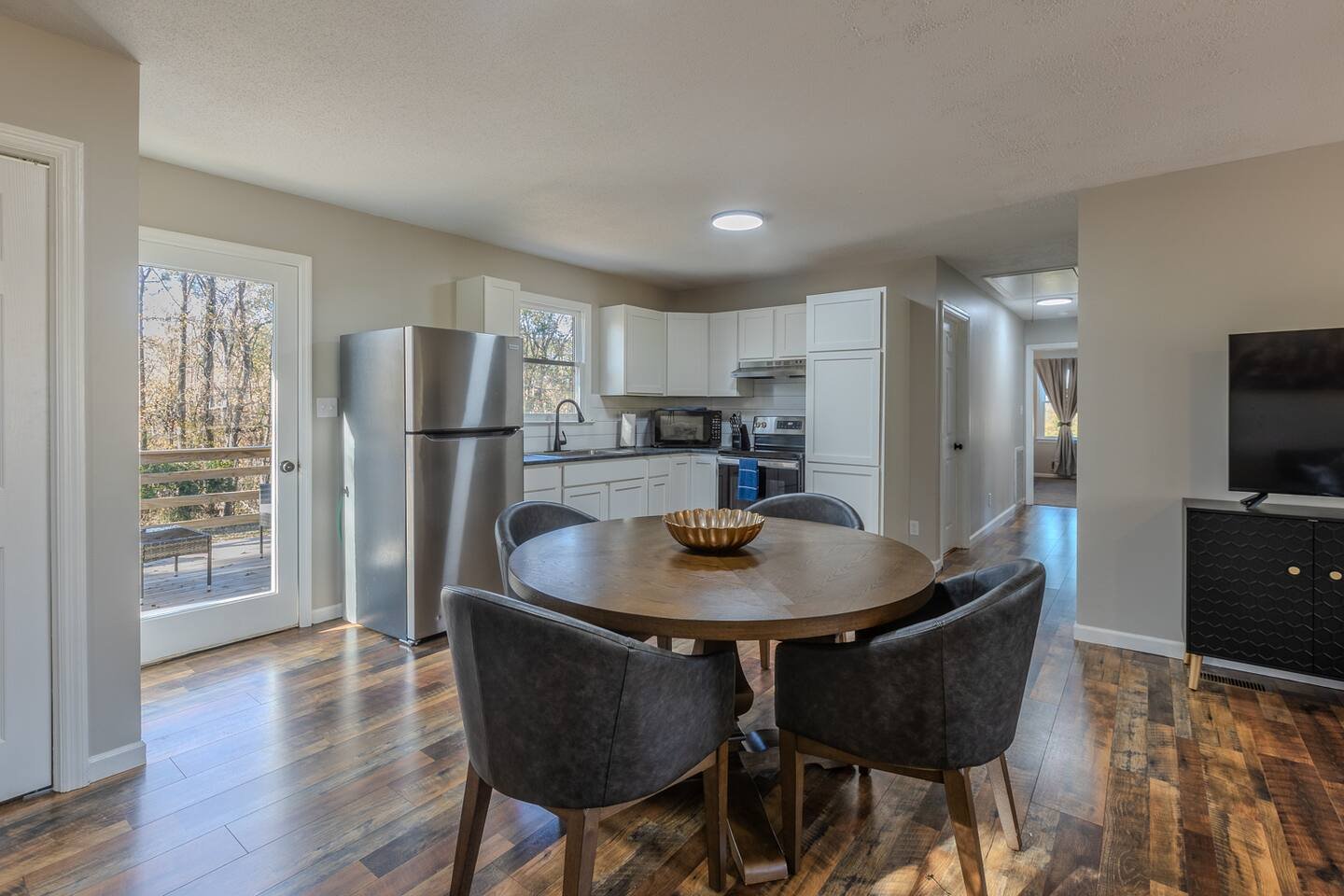 Kitchen and dining area with white cabinets, stainless steel refrigerator, microwave, oven, round wooden table with four chairs, and hardwood flooring.