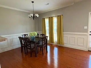 Empty dining room with a wooden table and chairs, yellow curtains, a chandelier, and hardwood floors.