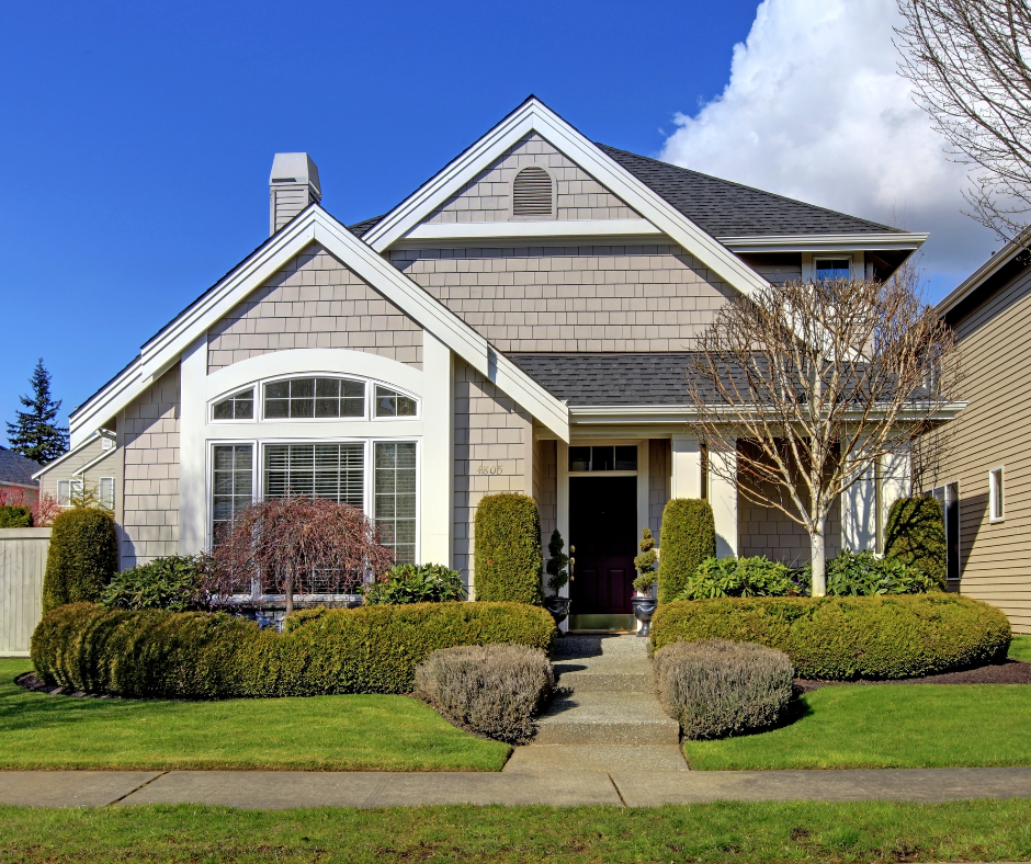 Front view of a two-story suburban house with a manicured lawn, shrubs, and leafless trees under a partly cloudy sky.
