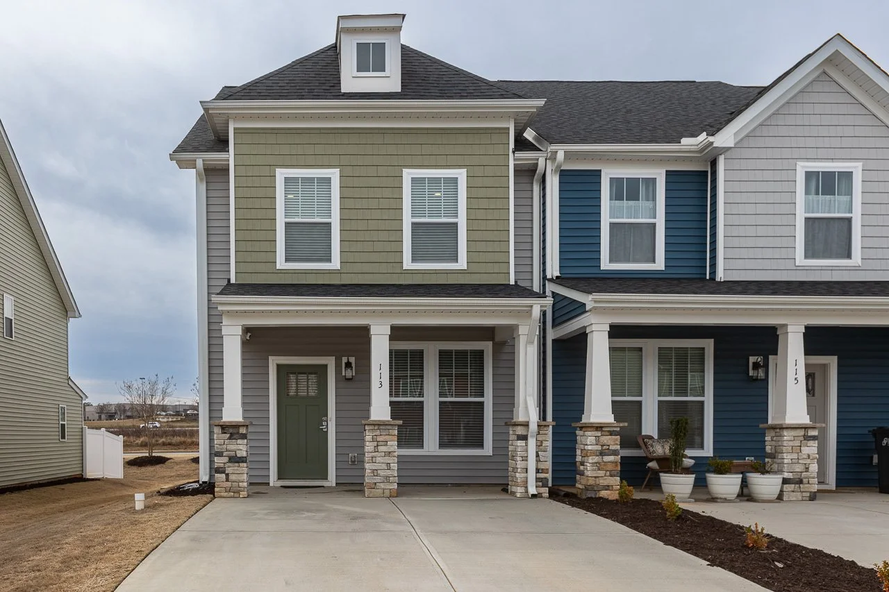 Front view of a modern multi-family house with colorful siding, stone columns, a driveway, and potted plants by the entrance.
