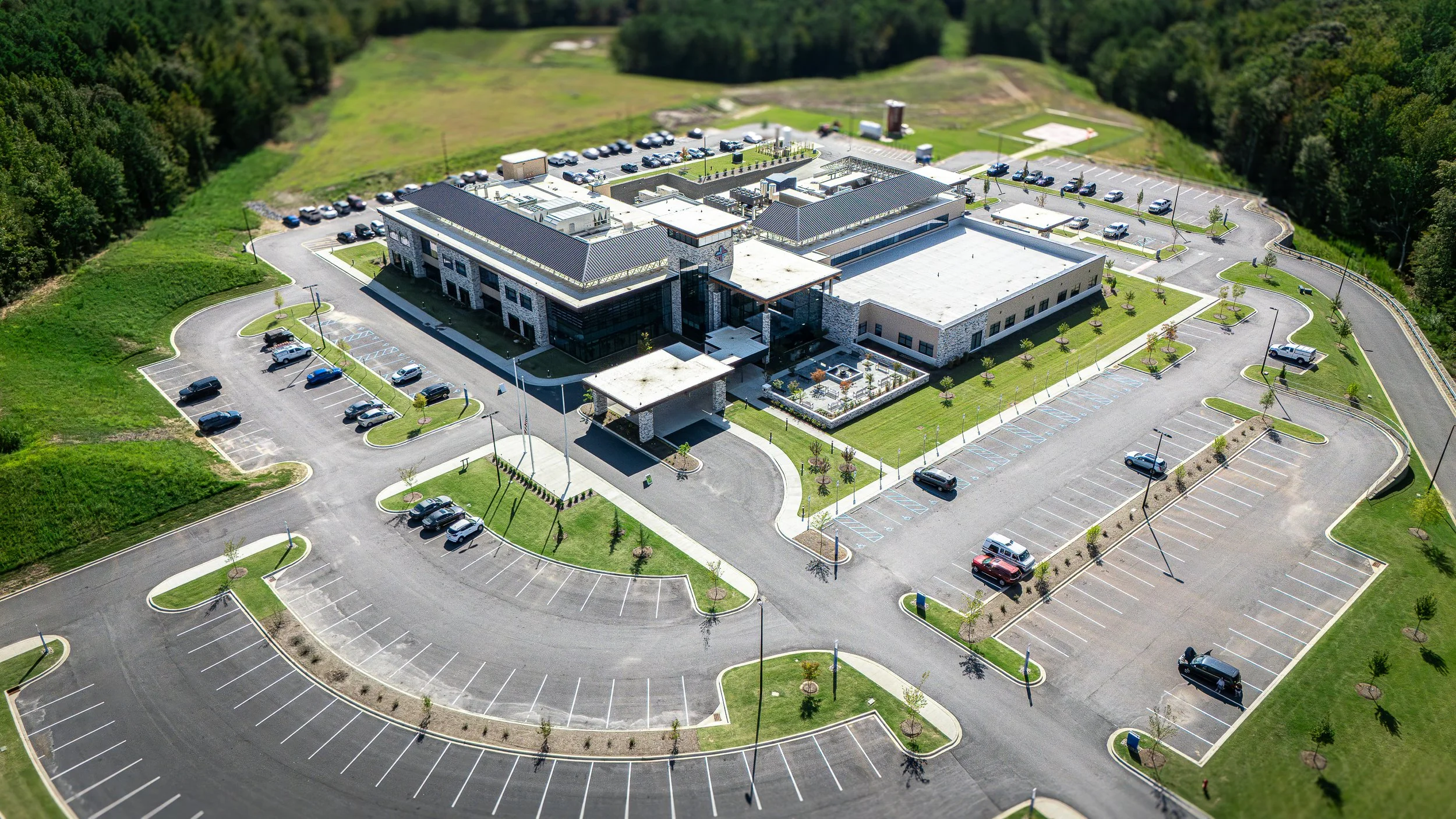Aerial view of a modern hospital building with a large parking lot and surrounding green lawns.