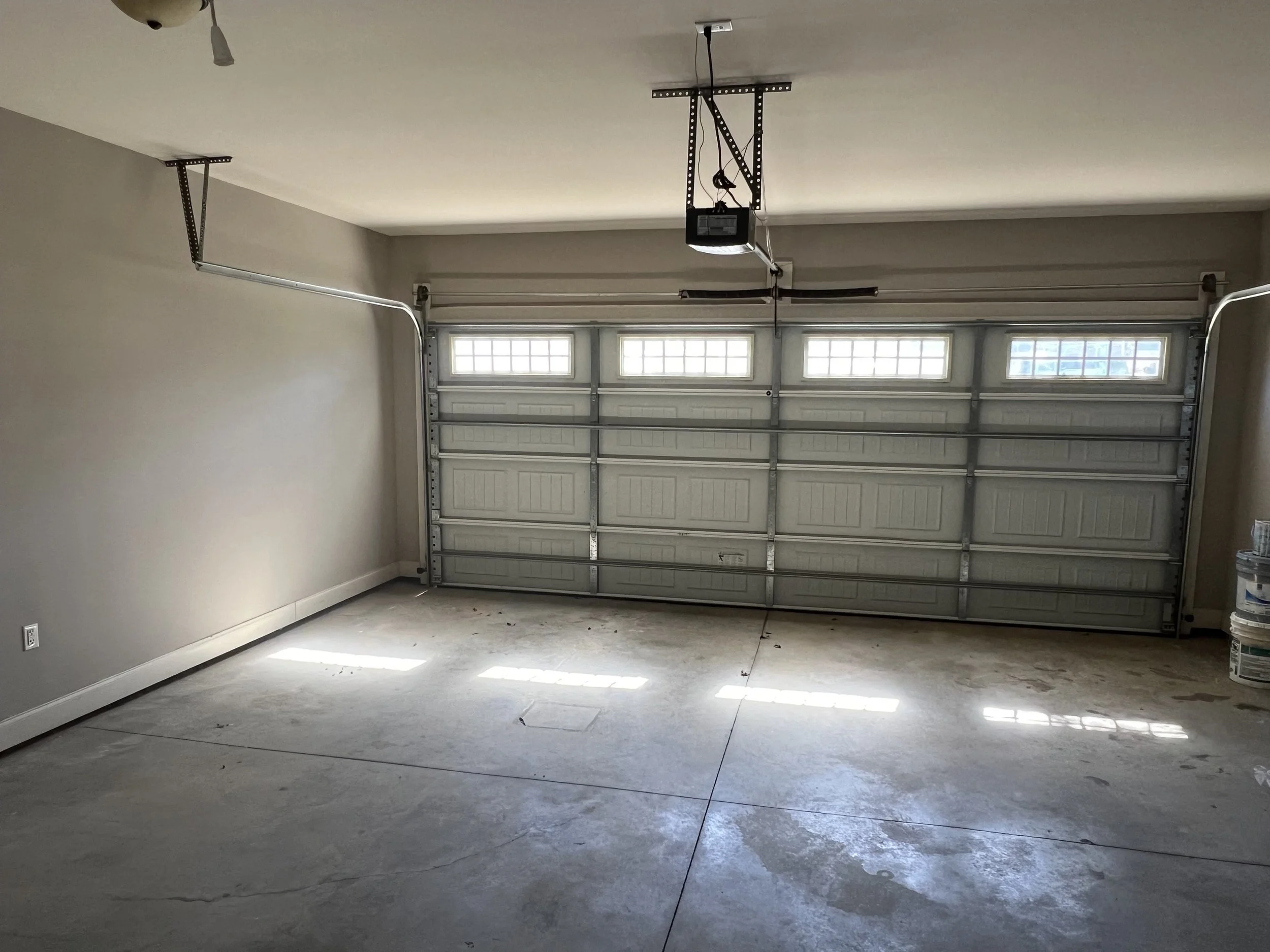 Empty garage with a closed overhead door and a partially open side window. The concrete floor shows some cracks and stains.
