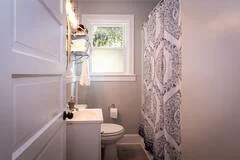 A small bathroom with a window, a toilet, and a patterned shower curtain.
