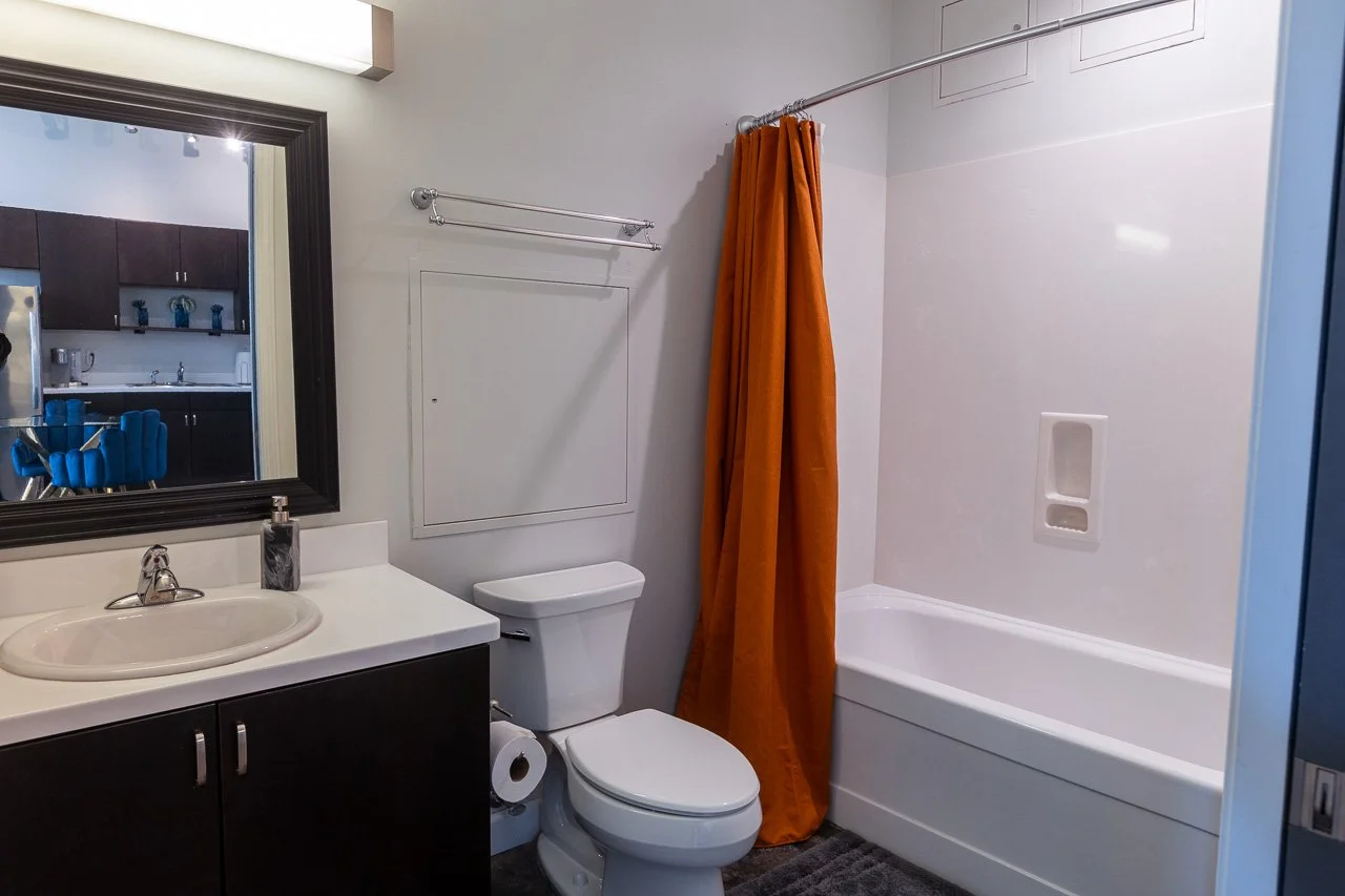 Bathroom with a sink, mirror, toilet, and bathtub with an orange shower curtain.