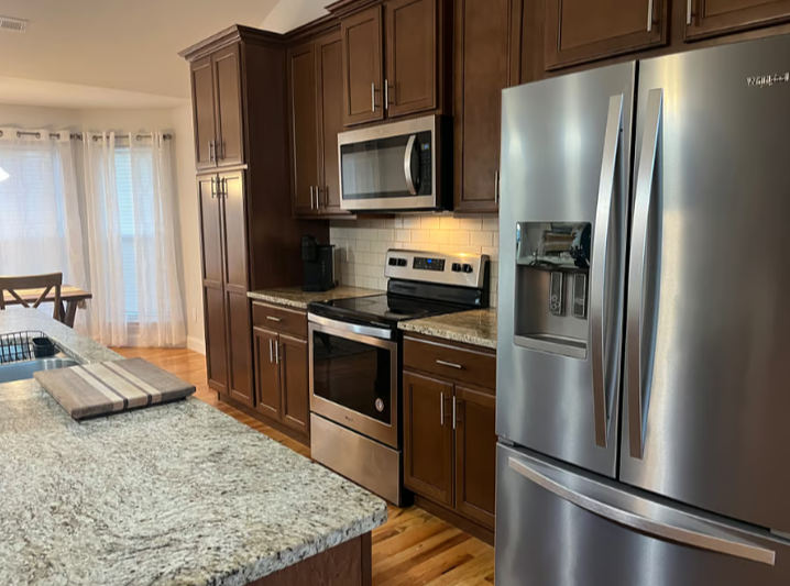 Modern kitchen with wooden cabinets, stainless steel refrigerator, oven, microwave, and granite countertops.