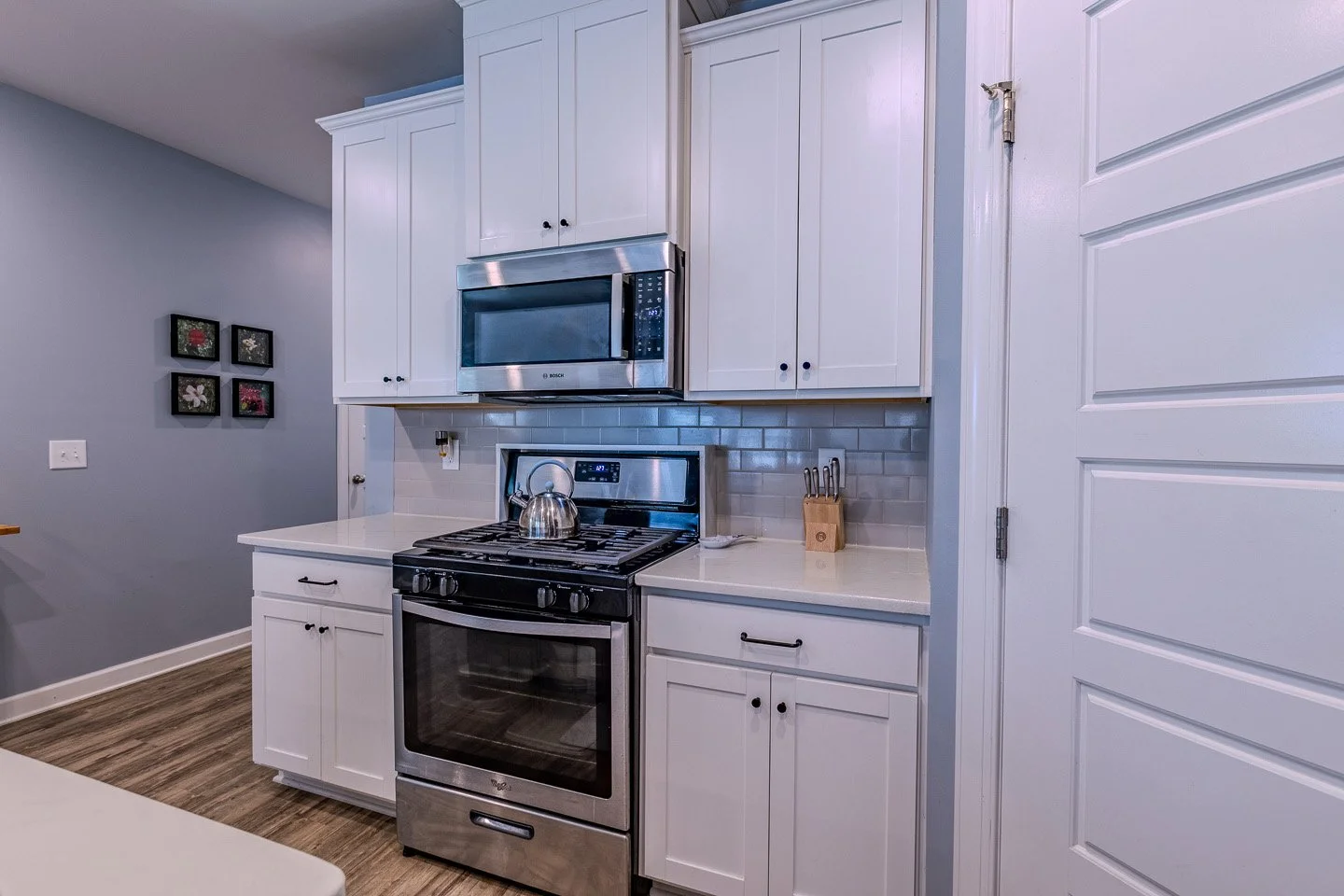 A modern kitchen with white cabinets, stainless steel oven and microwave, a tea kettle on the stove, a knife block, and artwork on the wall.