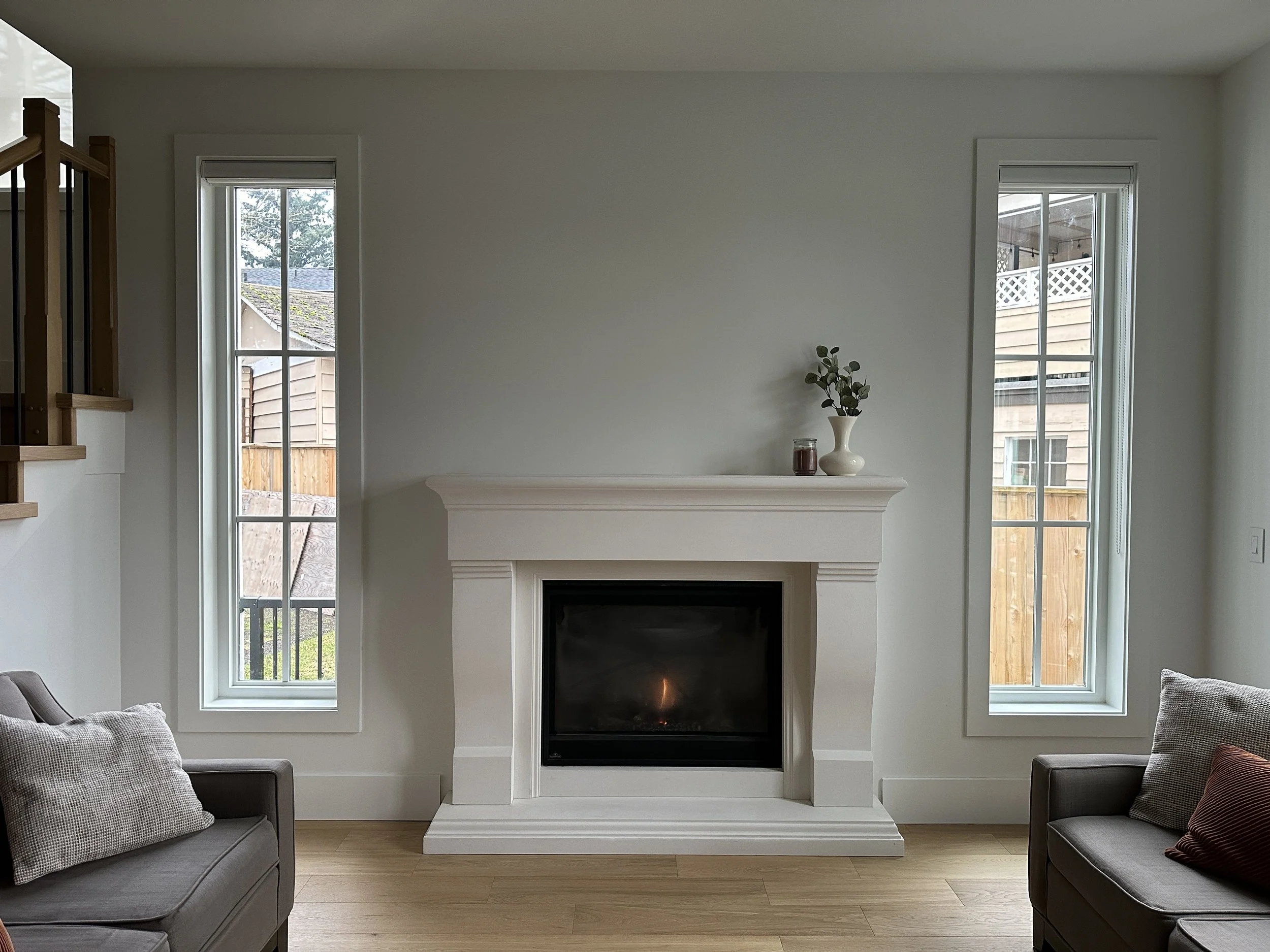 Living room with white fireplace, two tall windows on each side, two gray sofas, and minimal decor.