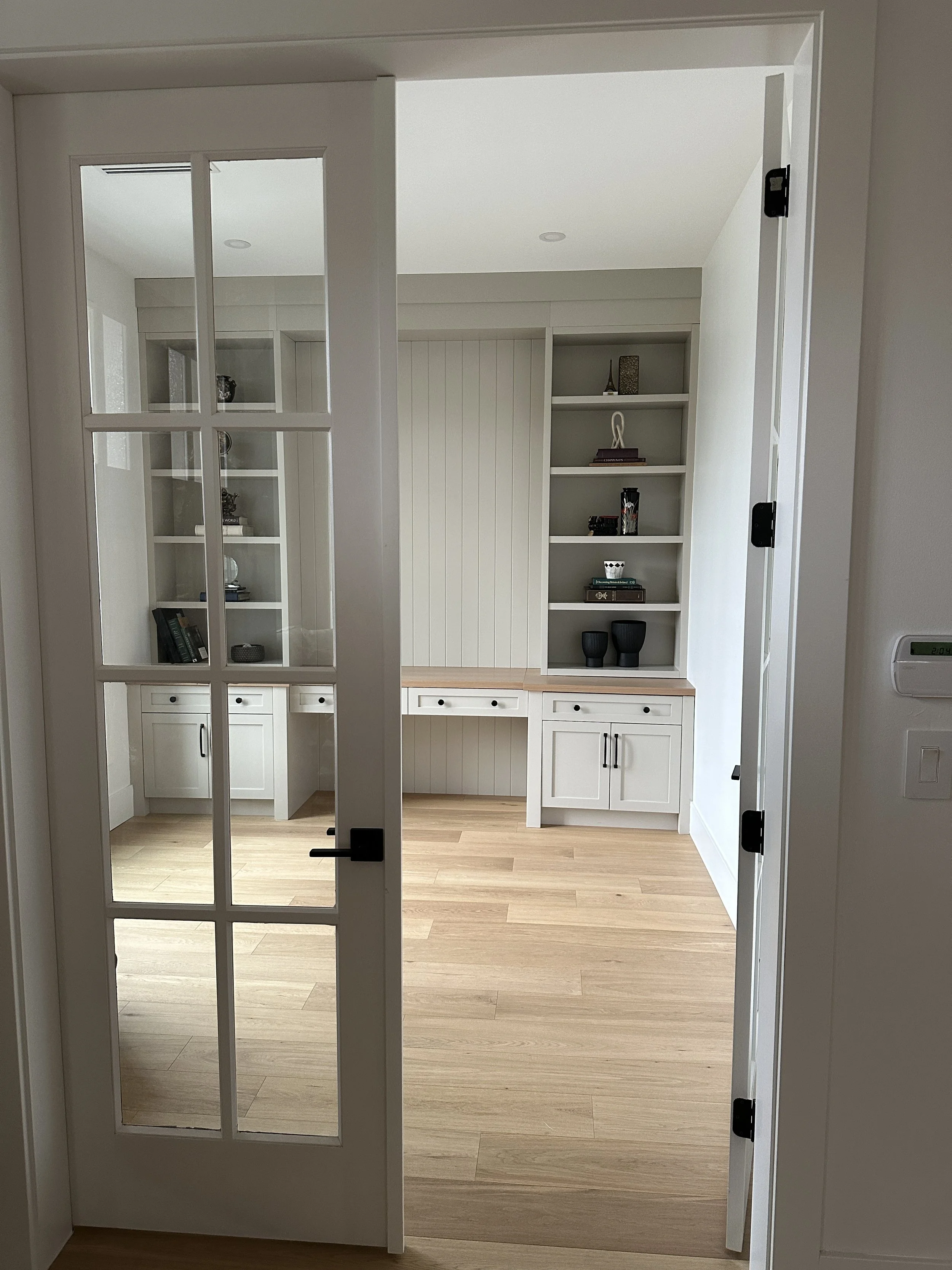 View through a glass-paneled door into a room with built-in white cabinetry and shelves, wooden flooring, and minimal decor.