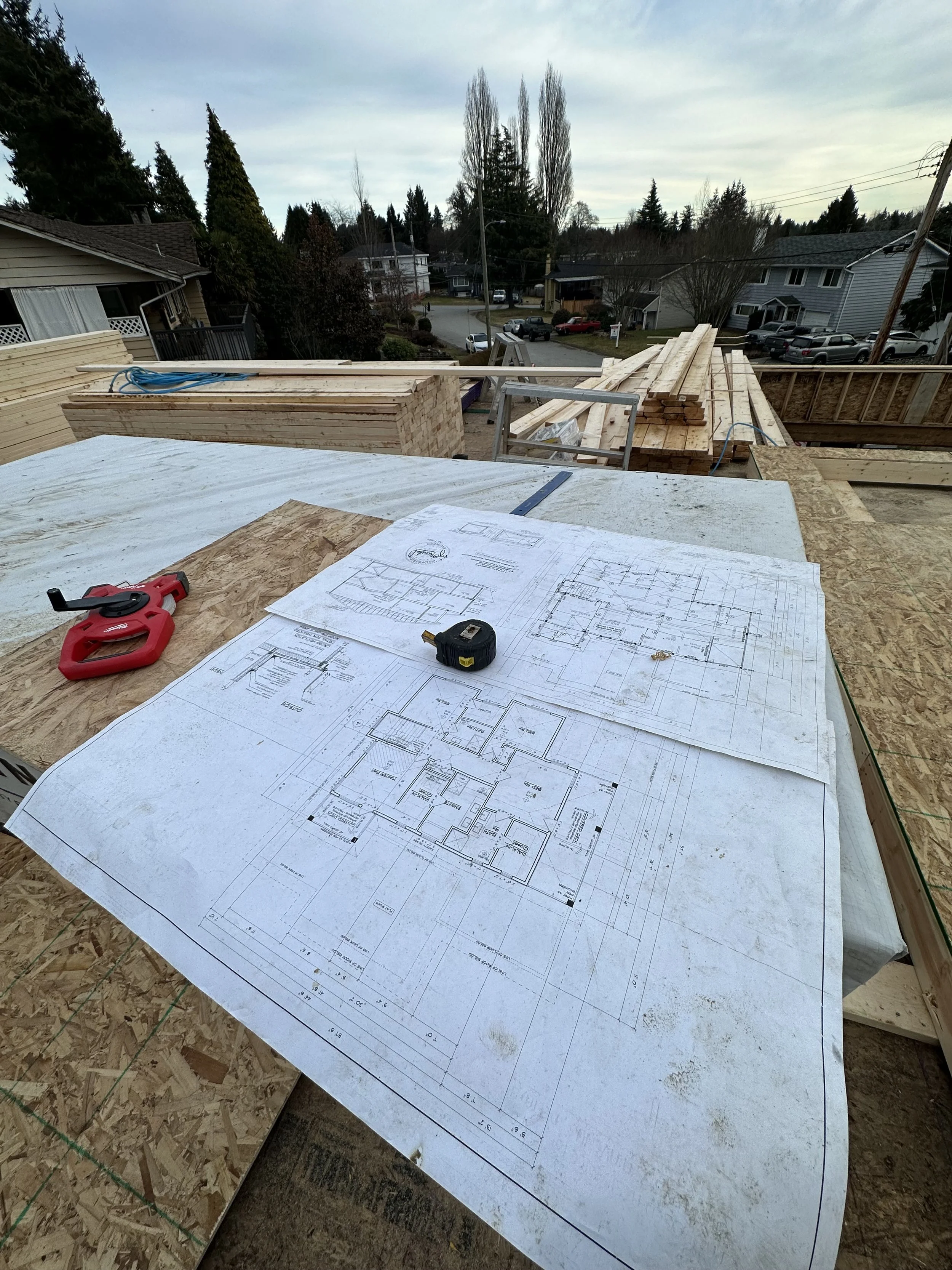 Construction site with architectural plans, tools, and wooden beams for building a house.