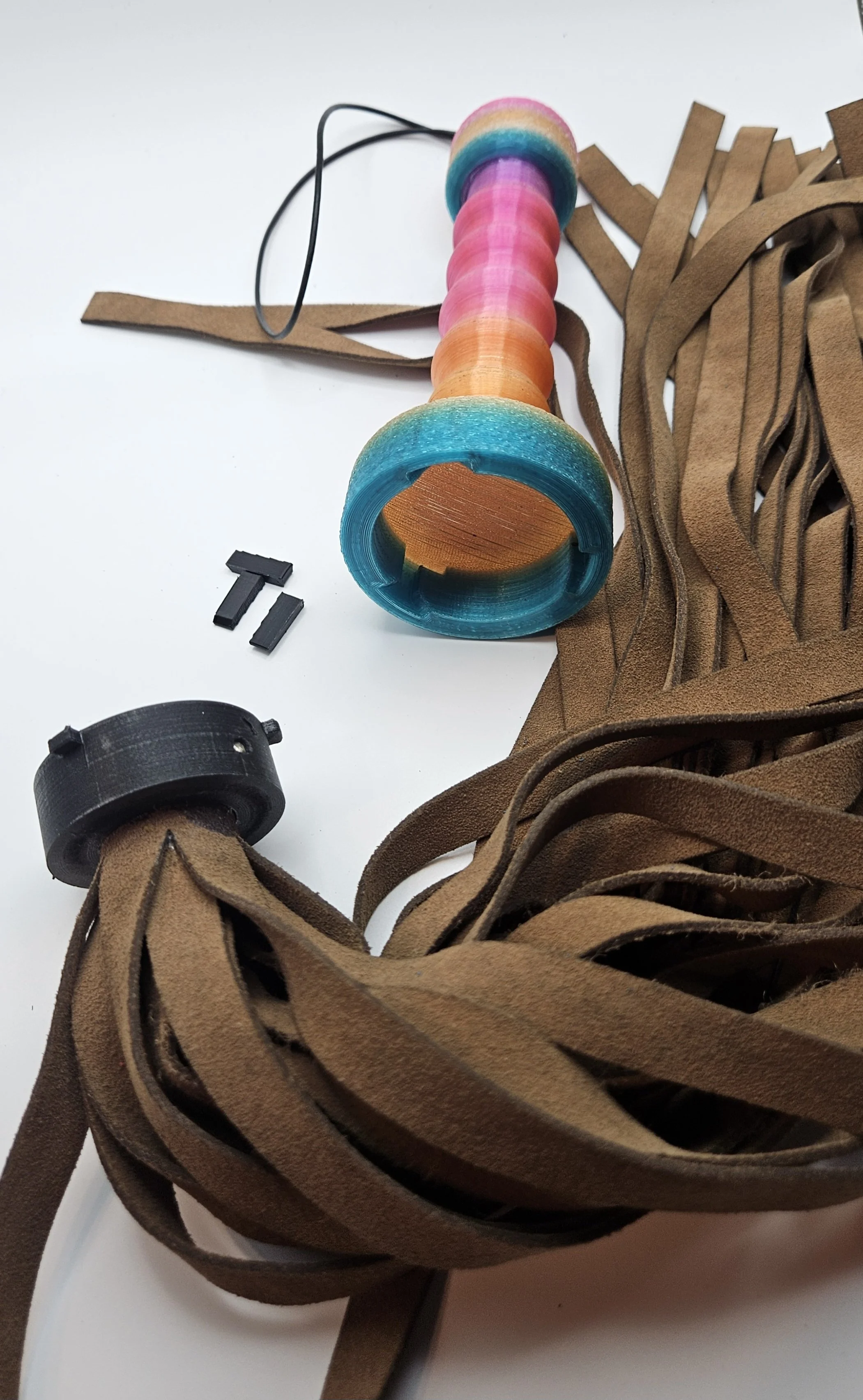 Colorful wooden and rubber components, brown leather strips, and small black plastic parts, likely parts for a craft or model project, are laid out on a white surface.