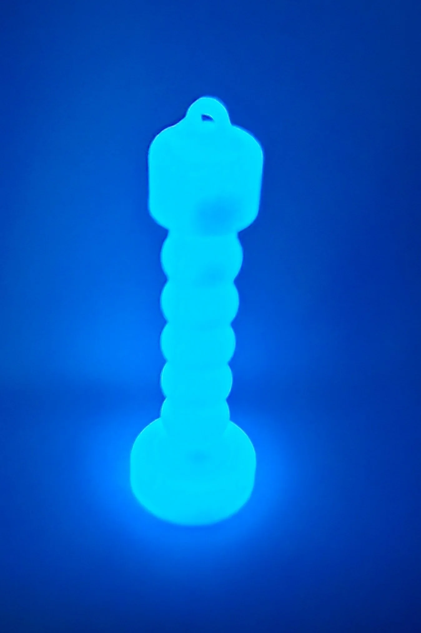 Glow-in-the-dark plastic toy shaped like a caterpillar with a segmented body and a loop at the top.