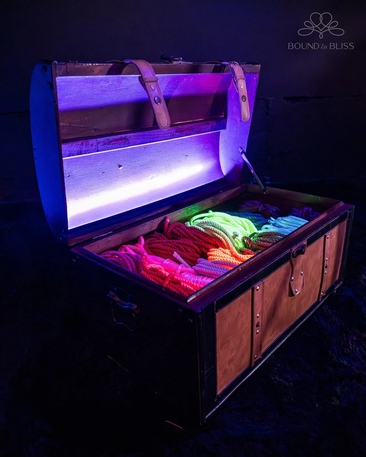 Open wooden chest filled with colorful glowing ropes in a dark room, with purple lighting.