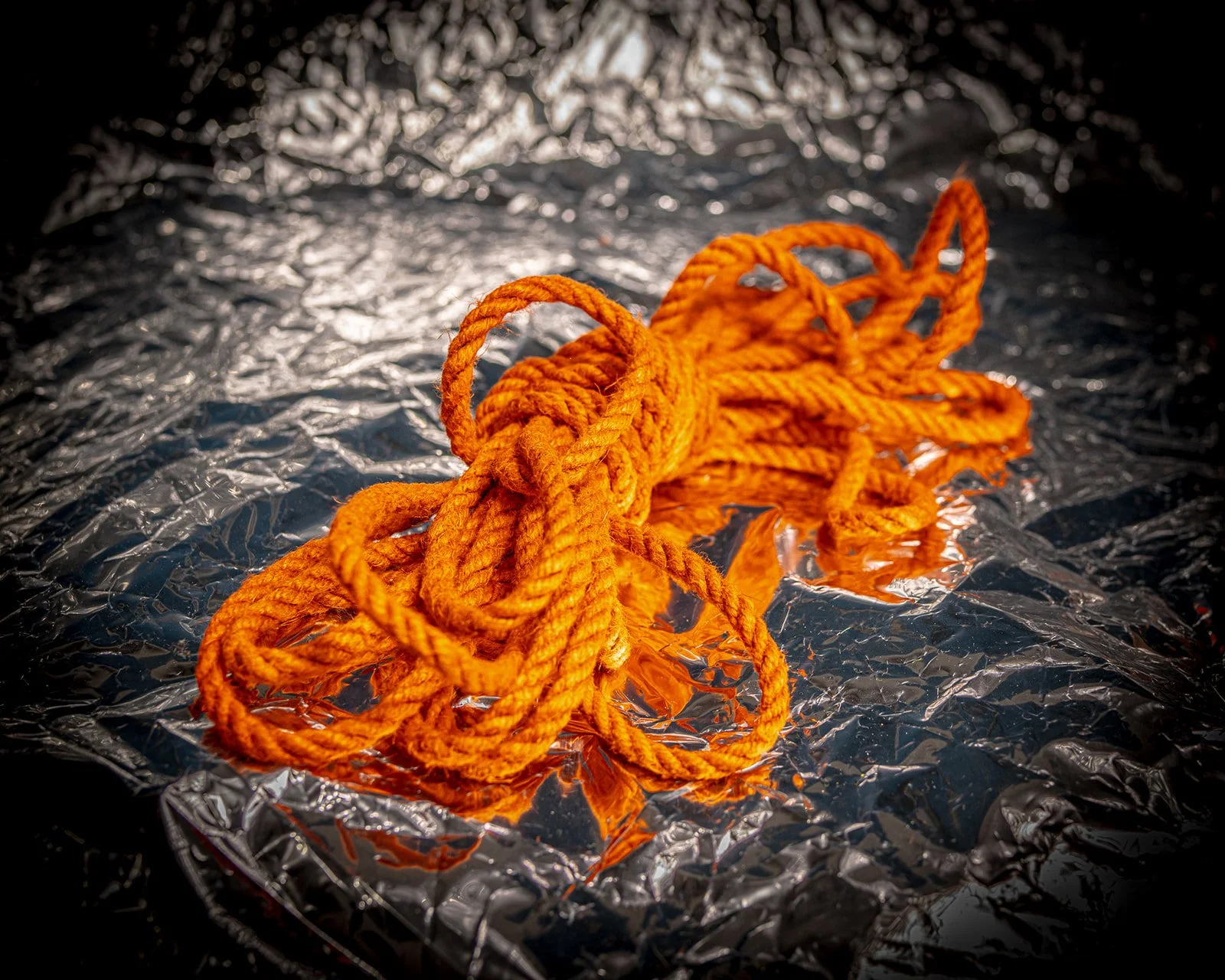 A tangled orange rope on a crumpled metallic foil surface.