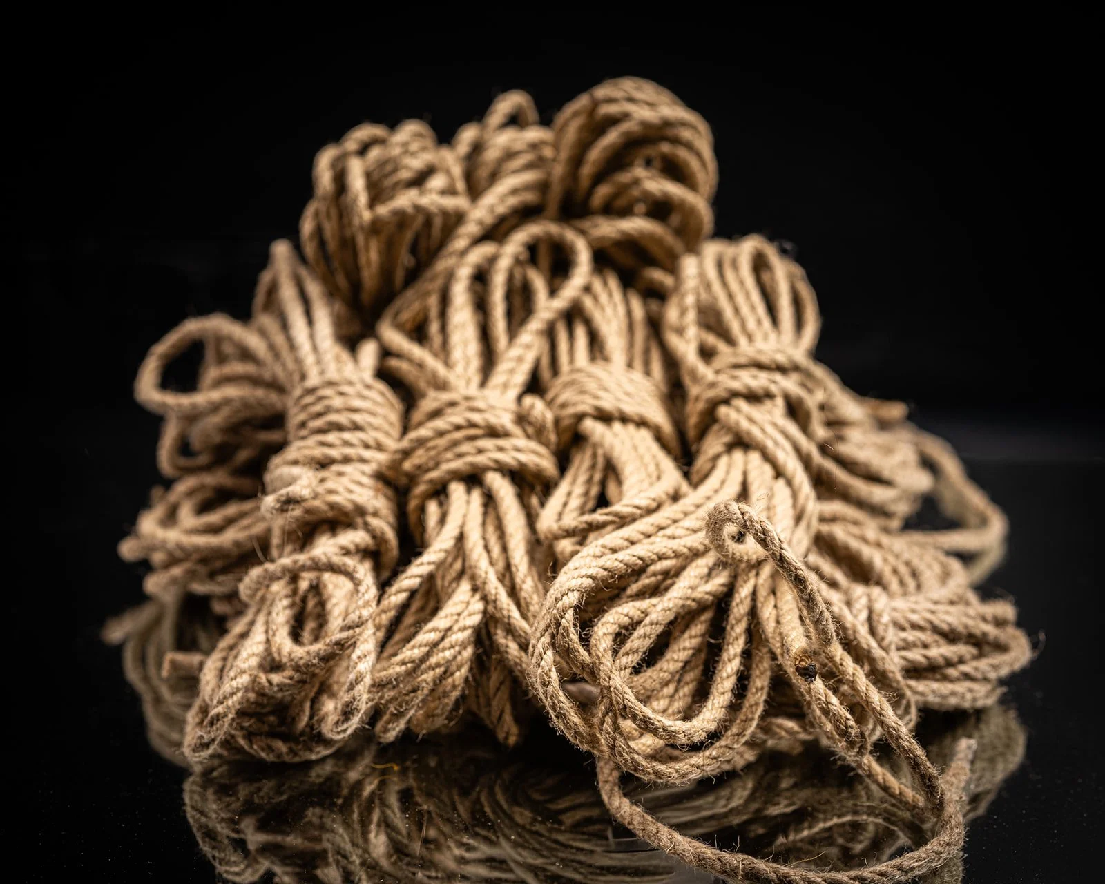 A tangled bundle of hemp, beige ropes or twine, resting on a black reflective surface.