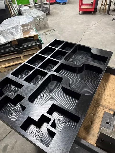 Black silicone mold with multiple cavities and spiral patterns, labeled 'CUP 4 P2 124', placed on a wooden workbench in a workshop.