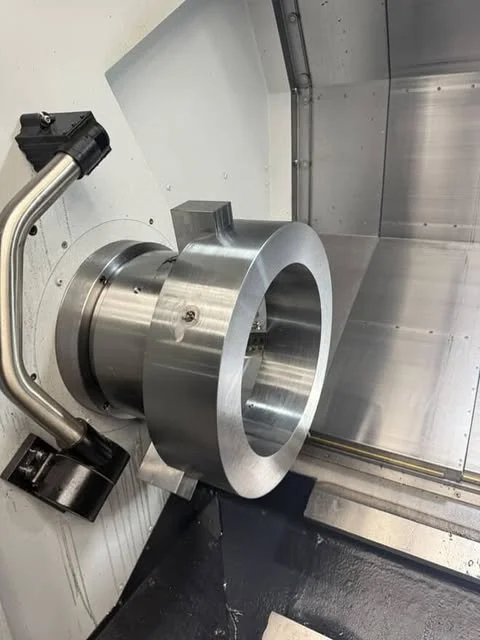 Close-up of a large, shiny metal rotational component inside a CNC machine or industrial equipment, with supporting mechanical parts and enclosure.