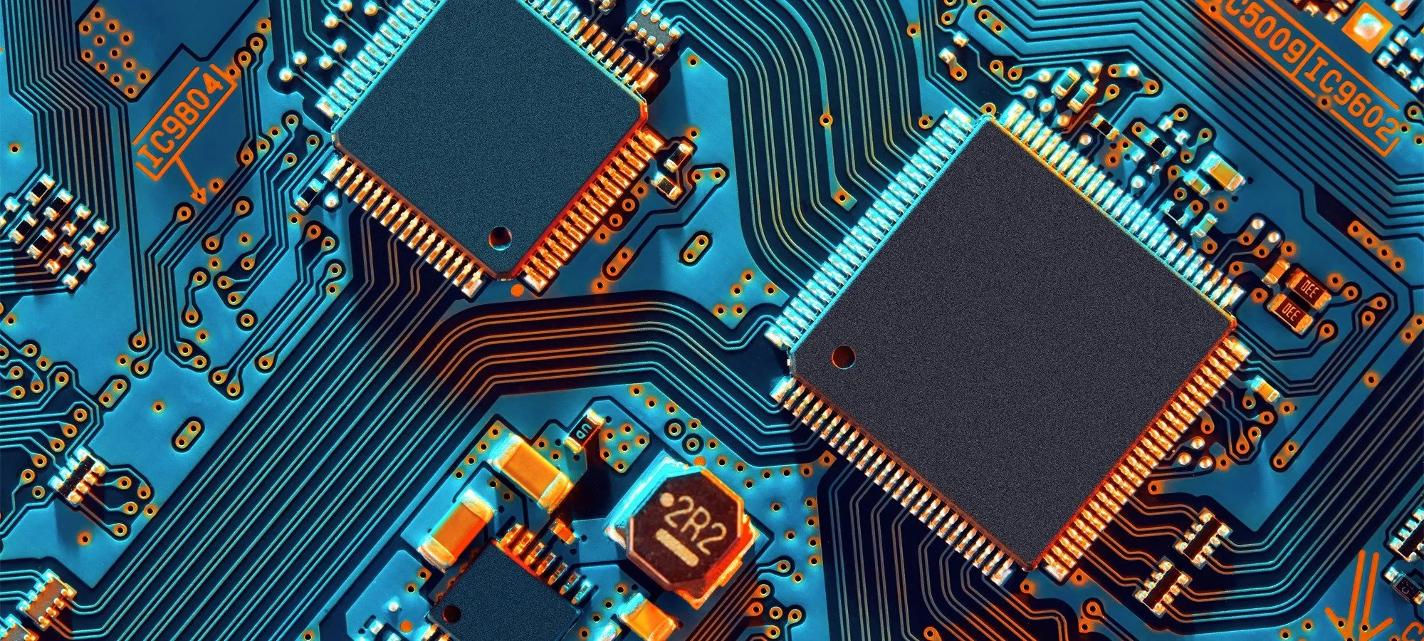 Close-up view of a blue printed circuit board (PCB) with various electronic components, including microchips, resistors, capacitors, and intricate circuit pathways.