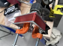 Close-up of a woodworking clamp holding a piece of red-painted wood in a workshop.