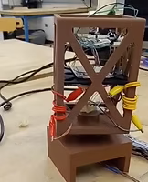 A small brown DIY electronic project with colorful wires connected to a circuit board, placed on a workbench.