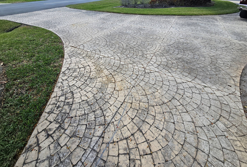 Curved concrete driveway with a decorative pattern and adjacent grassy lawn.