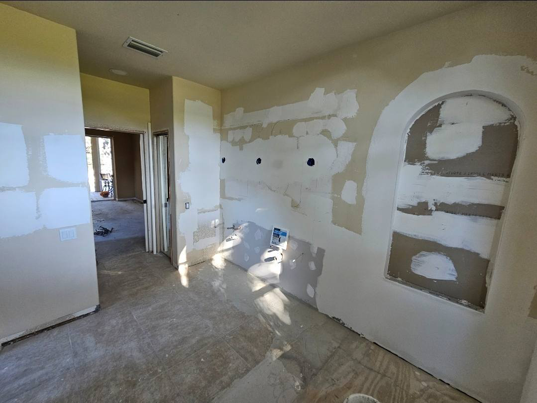 Room under renovation with drywall patches on walls, missing fixtures, and unfinished surfaces.