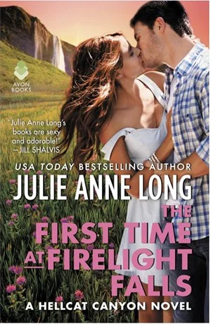 A romantic scene of a couple kissing outdoors with a scenic background of waterfalls, mountains, and a field of purple flowers. The book cover features the title 'The First Time at Firelight Falls' by Julie Anne Long.