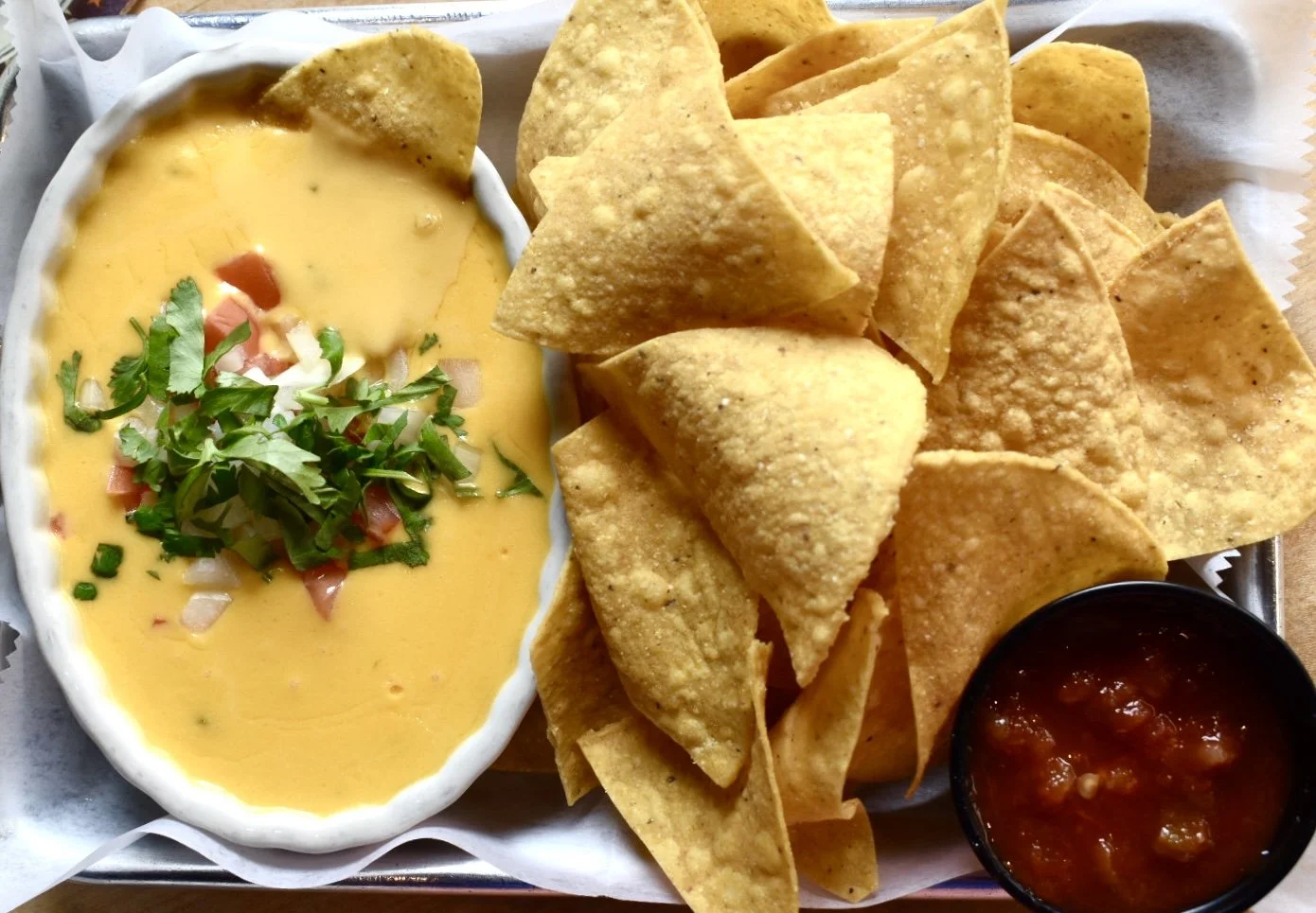 Cheese dip with diced tomatoes, onions, cilantro, tortilla chips, and salsa.