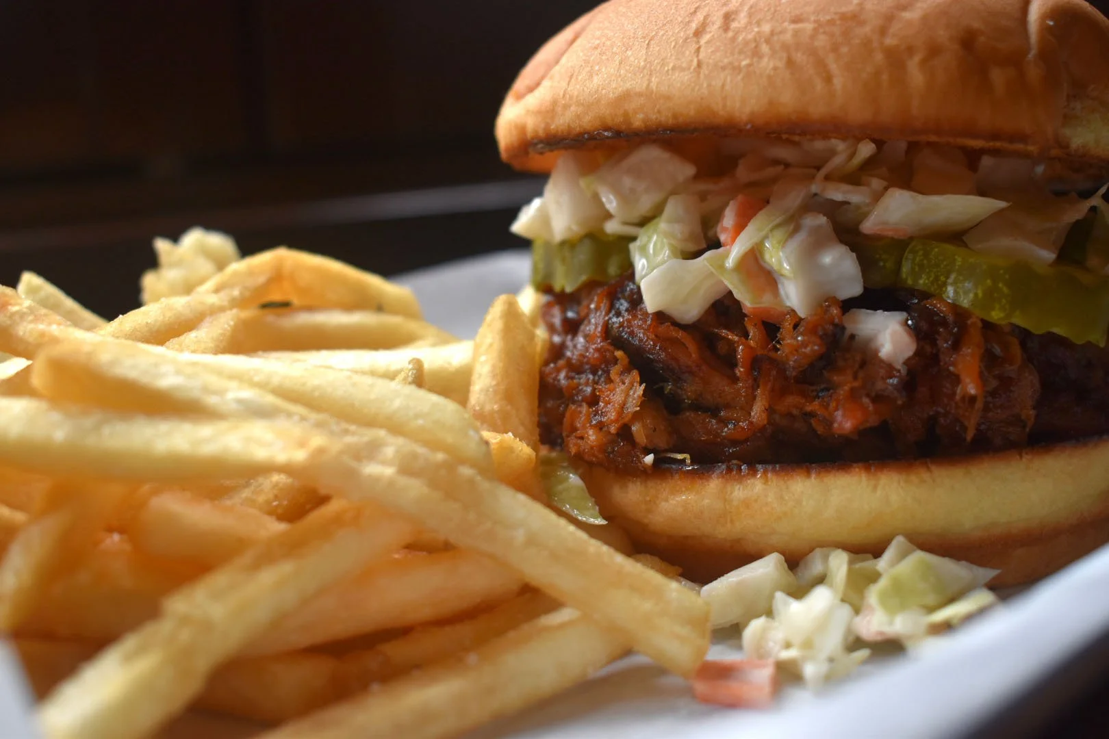 BBQ pork sandwich with coleslaw on a bun, served with French fries