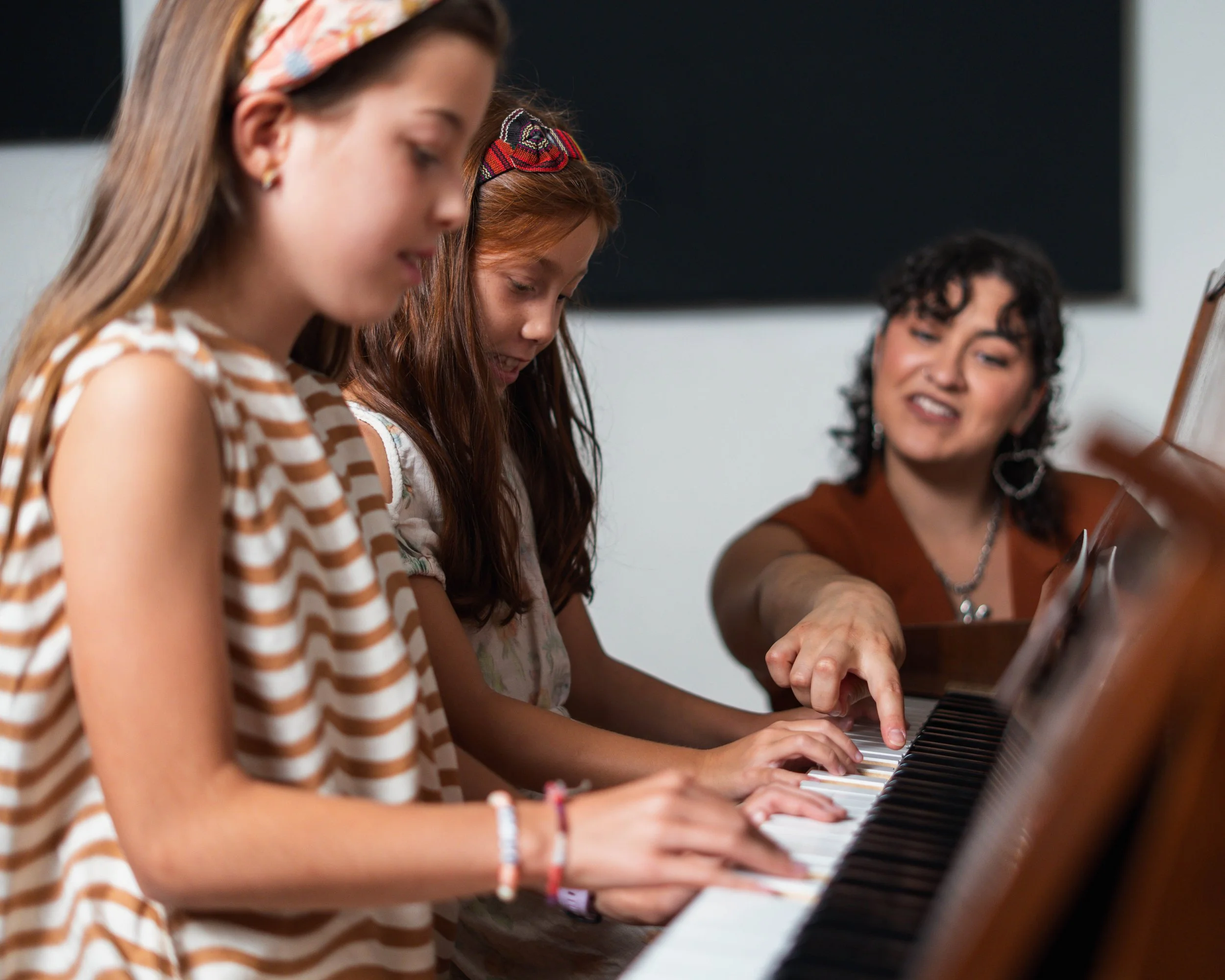 Two girls and a woman playing piano together in a music classroom.