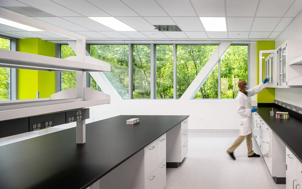 lab worker in a clean white lab with green foliage beyond windows