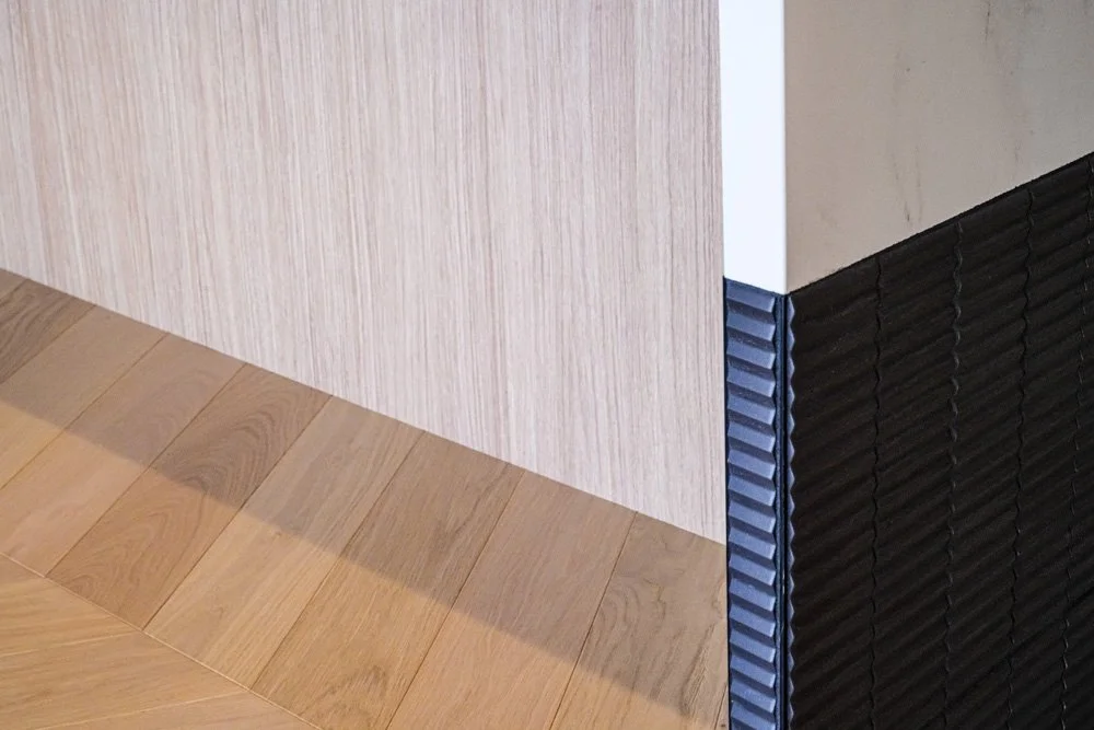 detail of kitchen island side showing white countertop, black tiles, and wood paneling and flooring
