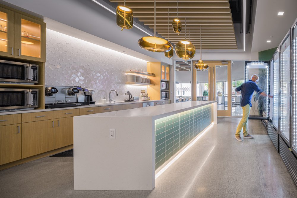 Kitchen / snack area in a modern office, with luxurious glass pendant lights, and man reaching into a refrigerator