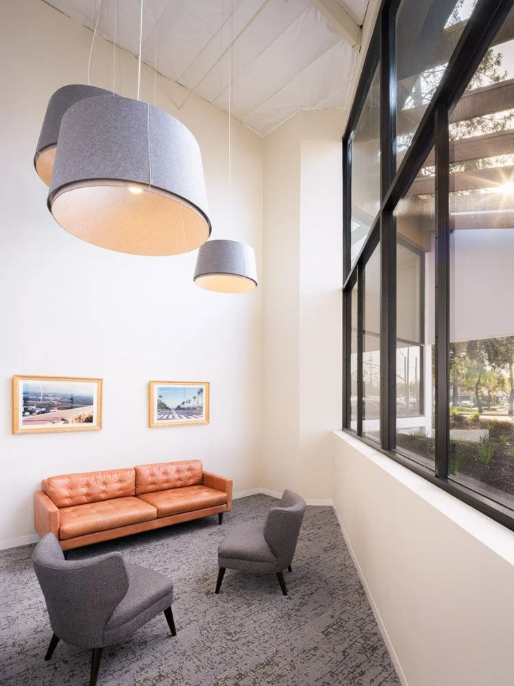 triangular room with pendant lights, large window, leather couch and gray chairs
