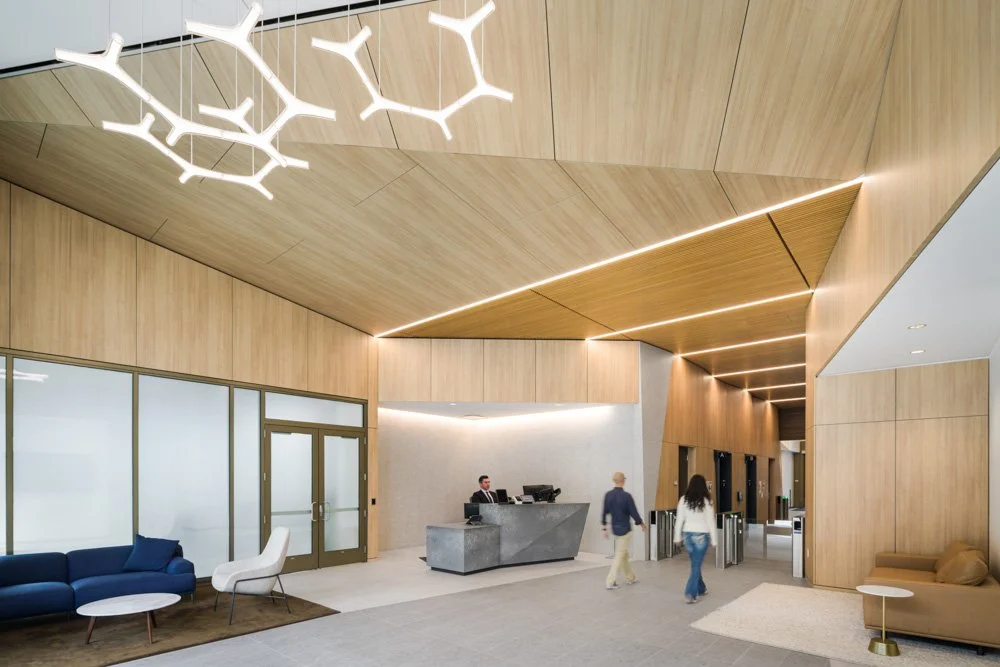 spacious lobby with geometric wood paneling, unique light pendant, security desk, two people walking