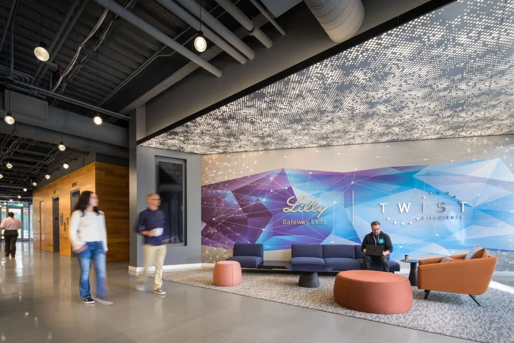 modern office lobby with perforated ceiling, geometric colorful mural, four people