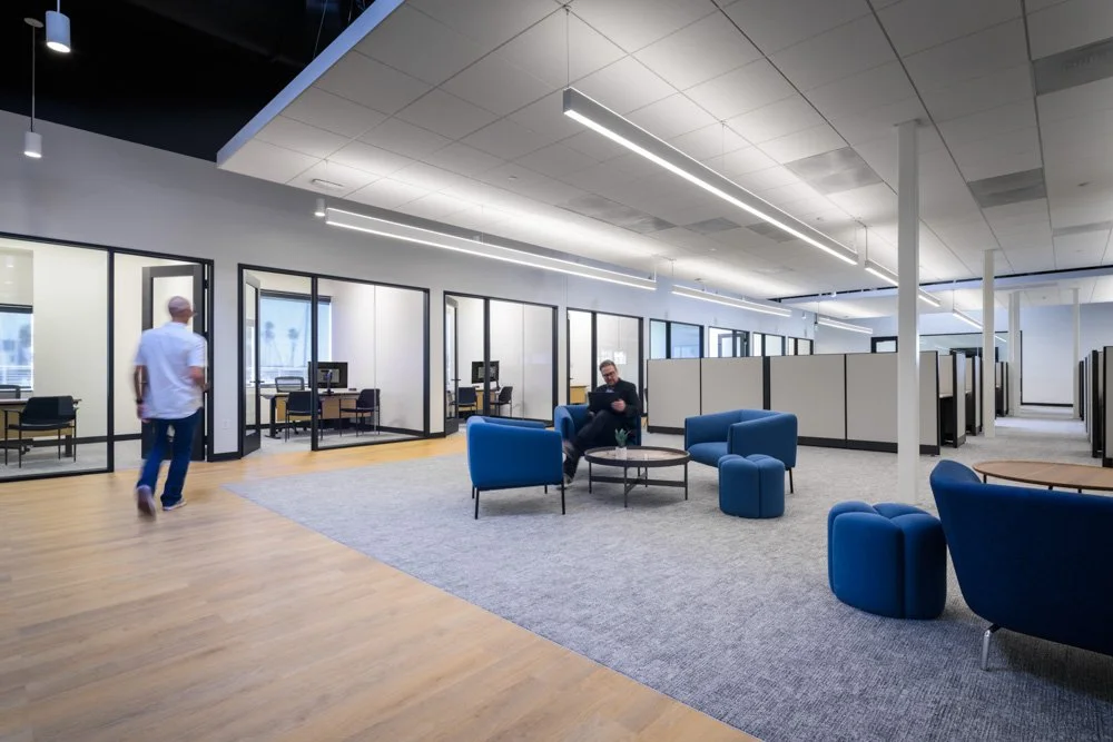 open office with lounge area, wood floor and gray carpet, two workers