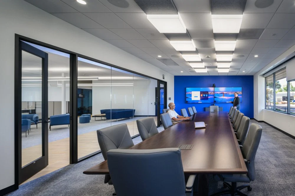 conference room with blue accent wall, large wood table, two workers, square light fixtures
