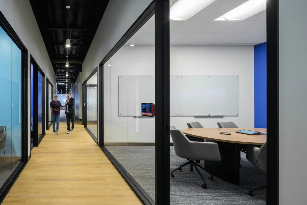 office corridor with small conference room, glass partitions, two men walking