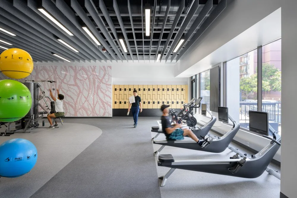 modern gym with rowing and weight machines, lockers, and acoustical ceiling baffles