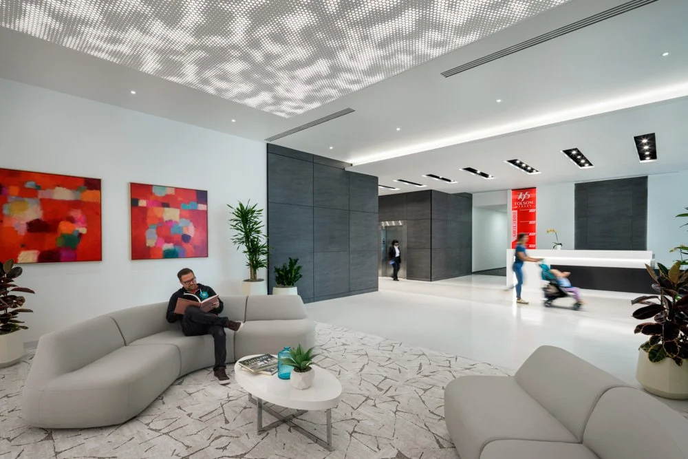 modern office building lobby with lounge area, curved sofas, perforated backlit ceiling and gray stone panels