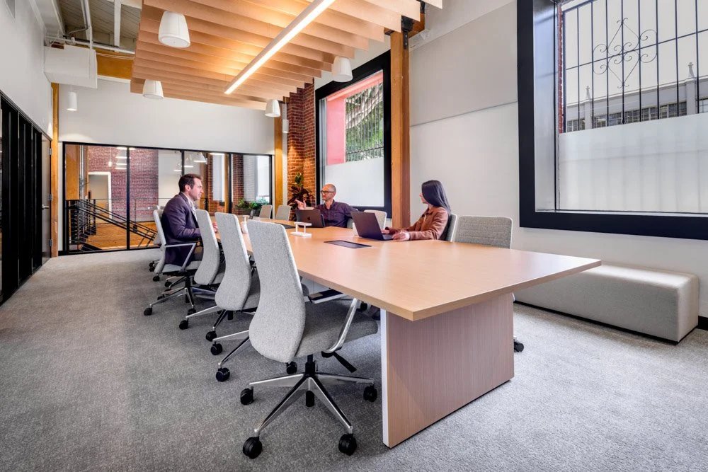 modern conference room with brick wall and glass partitions, three workers at conference table