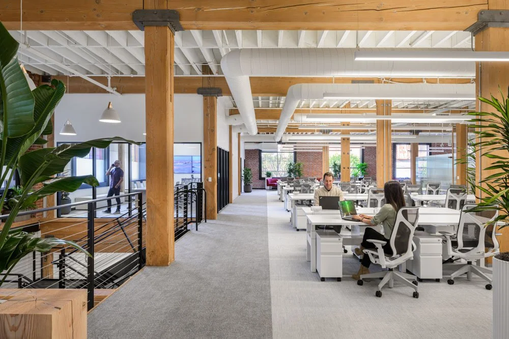 open office with timber columns, brick walls, plants, and three workers
