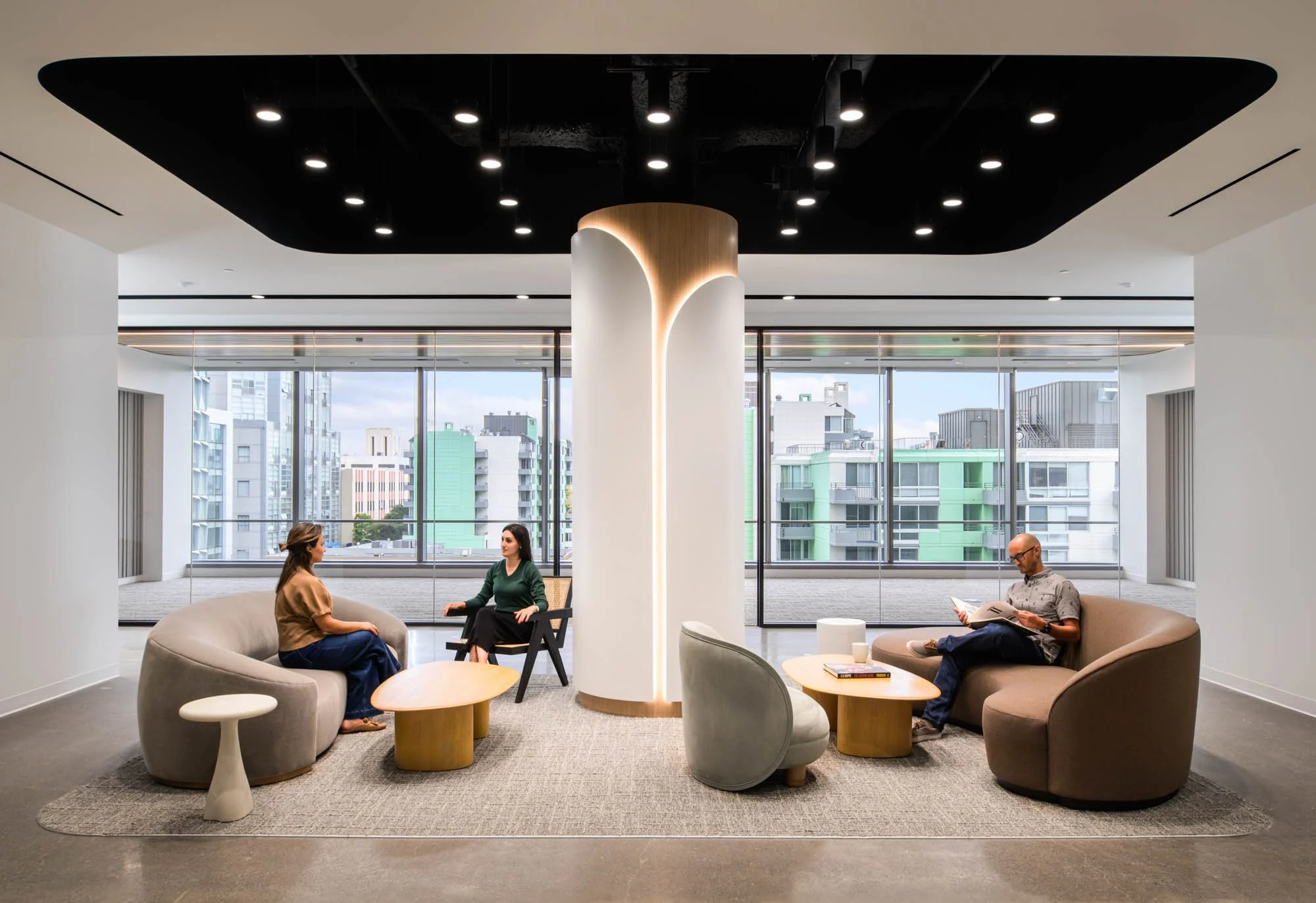 office lobby with central round column, lounge furniture, muted colors, and three people sitting