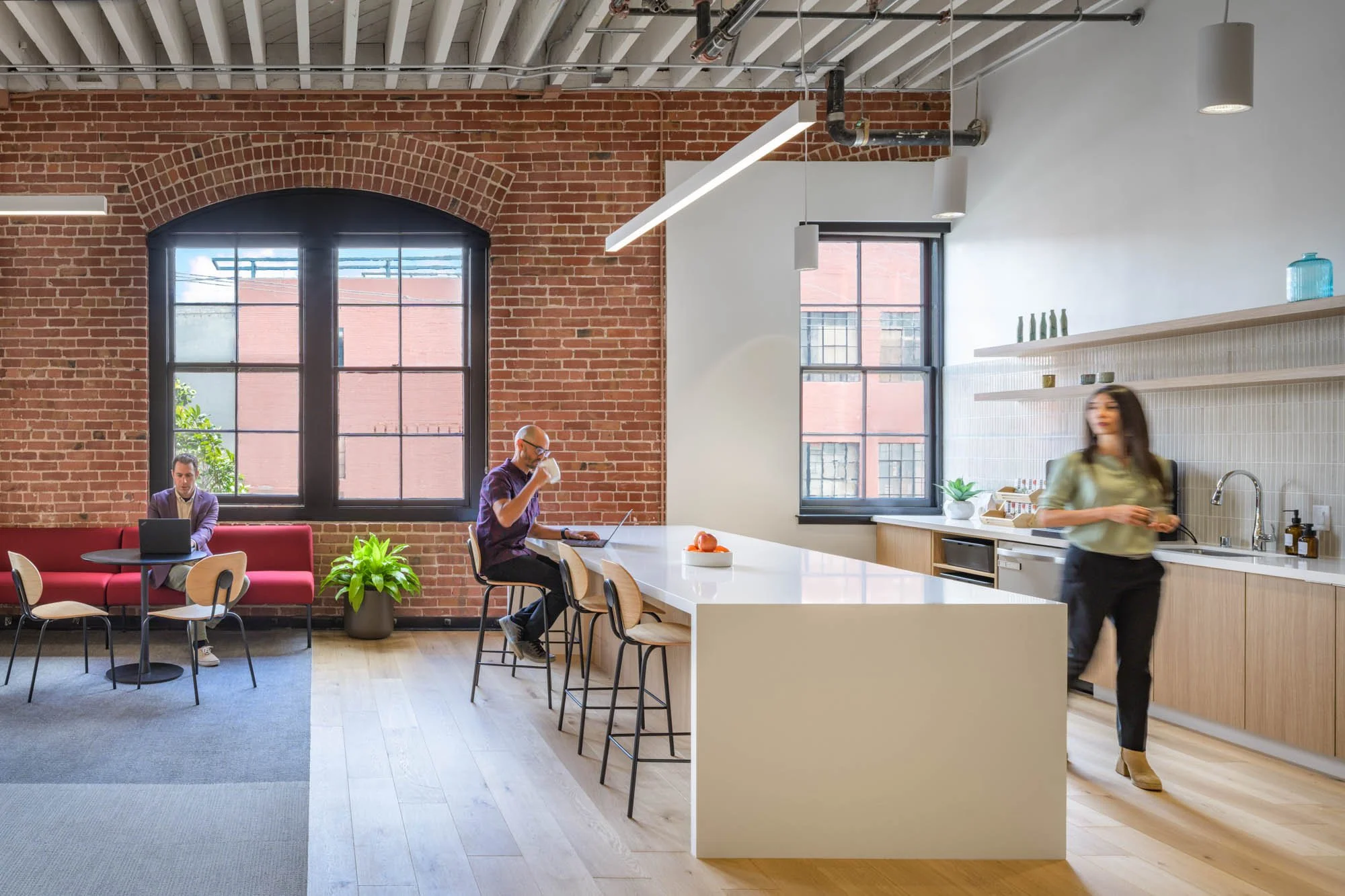 modern office kitchen and break area with brick wall, waterfall island countertop, neutral beige and white colors, three people