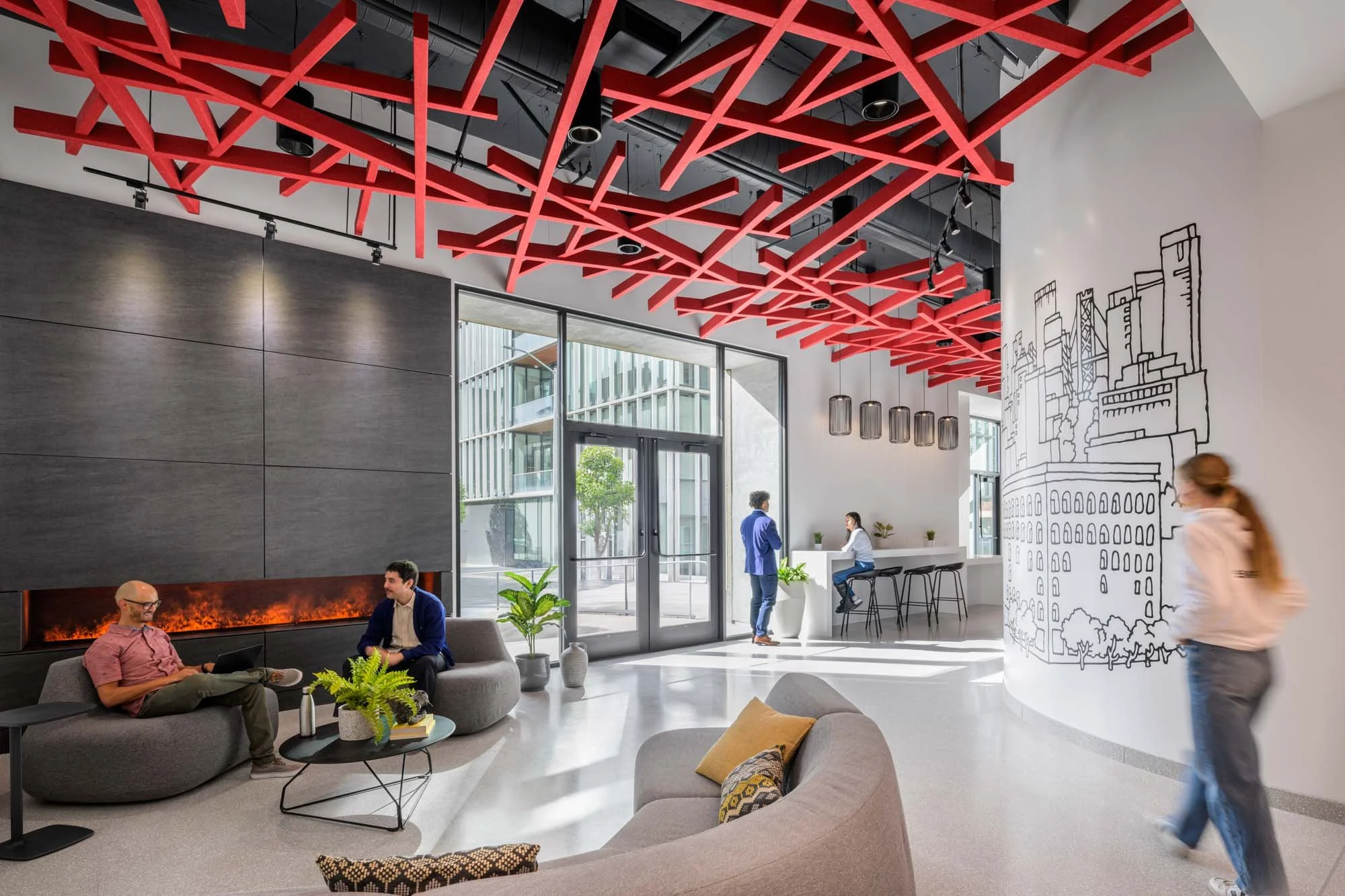 modern office lobby with lounge, red geometrical ceiling cloud, graphic mural, fireplace, and five people in the space